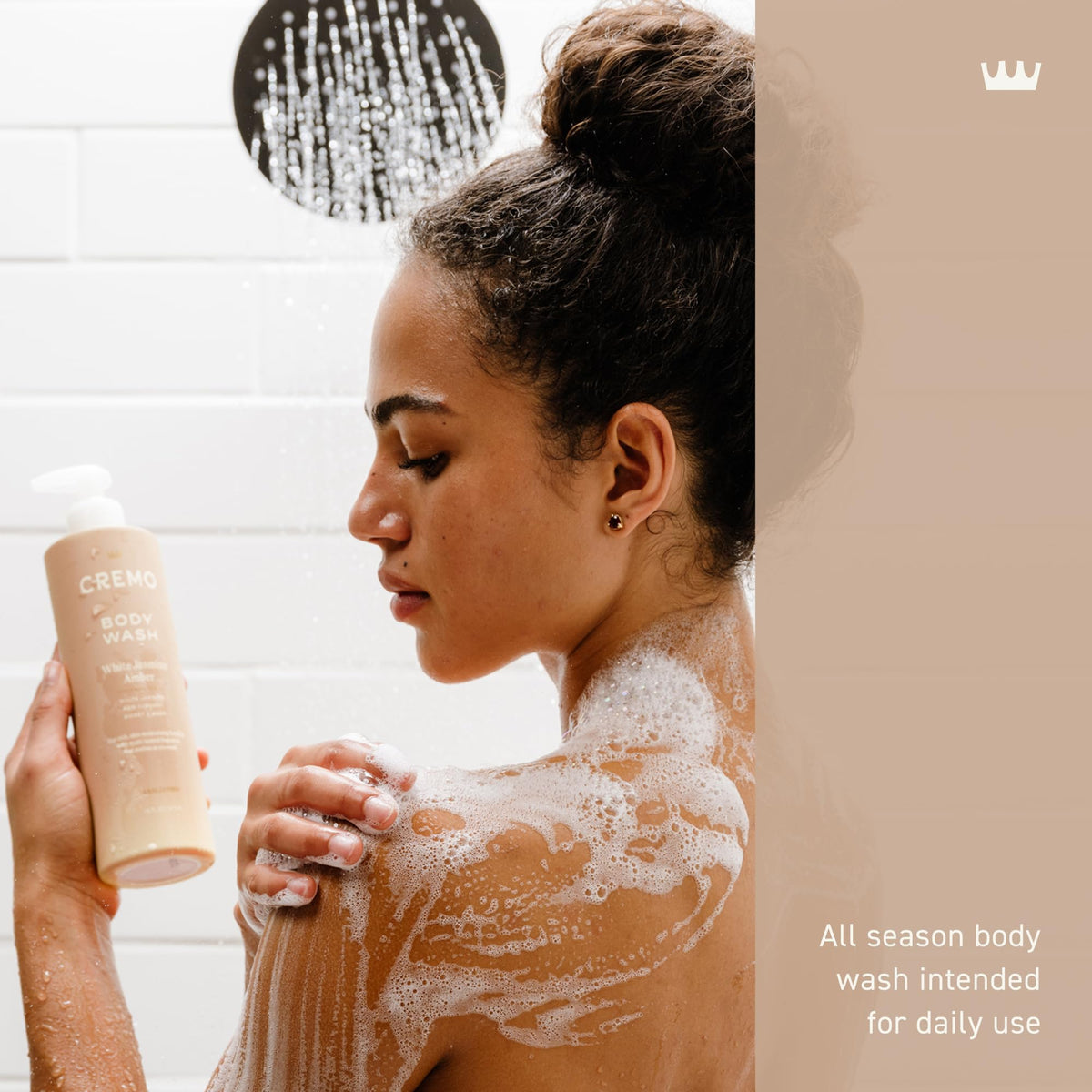 Woman applying CREMO body wash with a shower head in the background