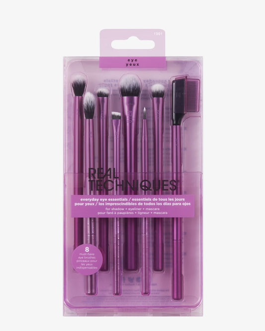 Real Techniques Everyday Eye Essentials makeup brush set in a clear plastic package with a purple hanger tab, containing eight brushes and an eye shadow applicator on a light gray background.